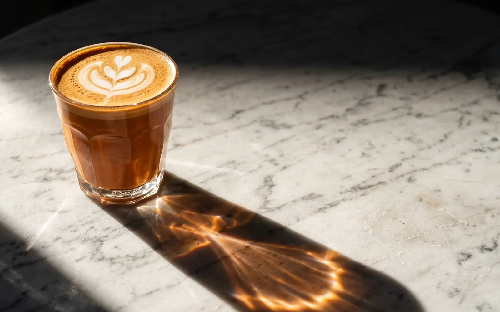 A cortado in a glass on a marble table, with a long shadow in the afternoon sun