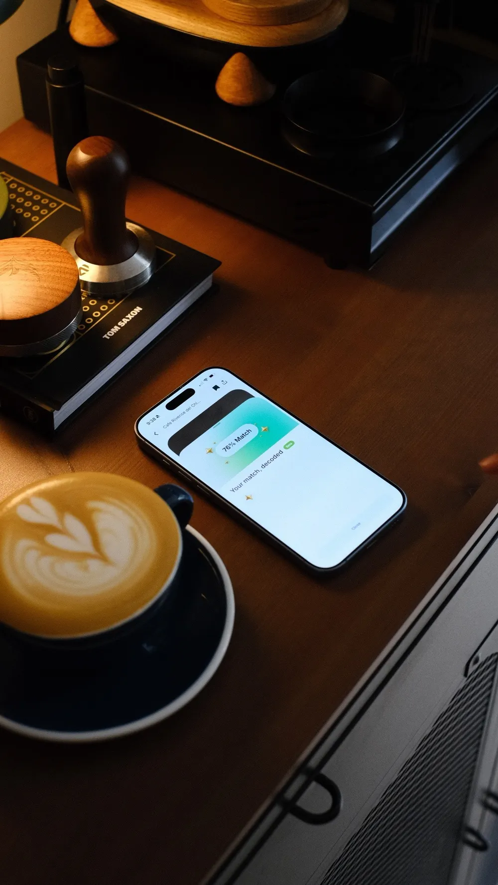 A latte on a wooden counter at home, with a phone lying next to it showing a Siip match