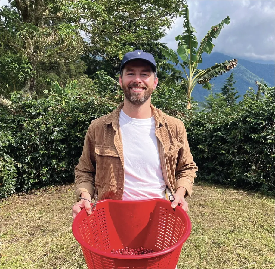Nick Spilger, founder of Siip, on a coffee farm holding a basket of coffee cherries